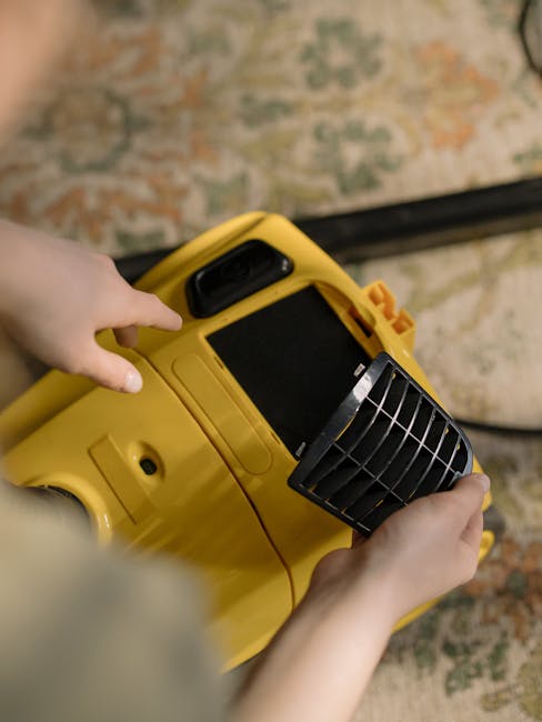 A person operating a yellow portable carpet cleaner with a black handle and vent, positioned on a patterned carpet in a room with beige and greenish tones. The scene shows the appliance's control pane